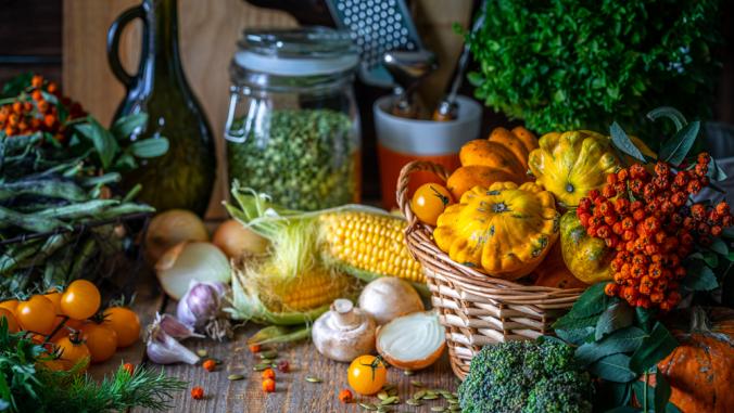 Autumn vegetables on a wooden table: pumpkin, orange pepper, paprika, mushrooms, corn, sweet potato yam, squash, cauliflower, broccoli tomatoes herbs basil