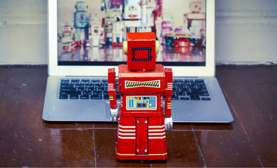 红色的玩具机器人看着打开的笔记本电脑