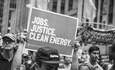 在2014年纽约人民气候游行中，一个人举着支持“就业、正义、清洁能源”的标语牌，黑白照片