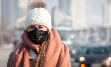 年轻女子戴着防护口罩在城市街道上行走，冬季雾霾和空气污染严重