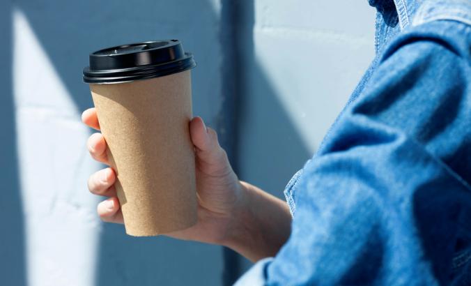 Person holding a disposable coffee cup. They are wearing a blue denim shirt.