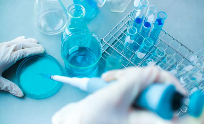 Person holding equipment — including beakers and a petri dish — in a chemistry lab