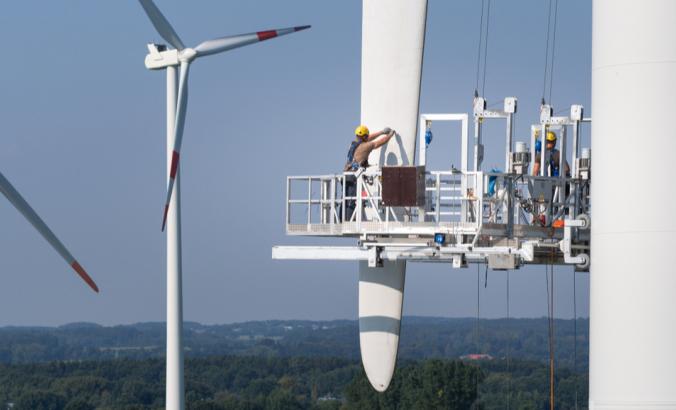  Workers on a hanging platform repair a damaged rotor blade on a wind turbine