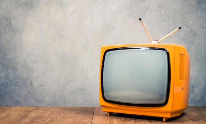 Retro old orange TV receiver on table front textured concrete wall background. 