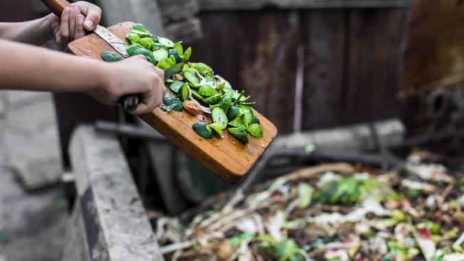 Person moving vegetable waste from cutting board to the garden compost heap