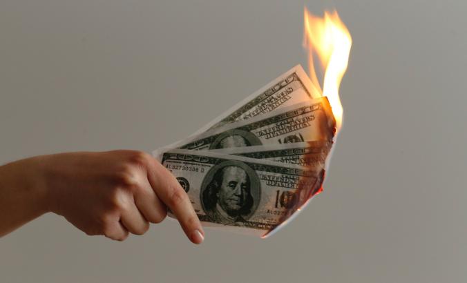 Person holds hundred dollar bills that are burning