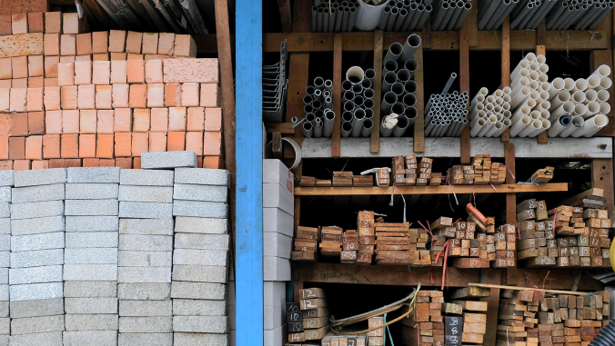 Construction building materials and industrial supplies such as bricks, woods and pipes stacked and arranged for sale at a hardware store front.