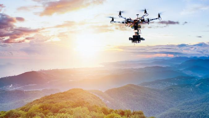 A photograph of a camera-equipped drone over a forest at sunset 