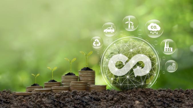 A green globe with circular economy icons on top of soil next to a stack of coins with 